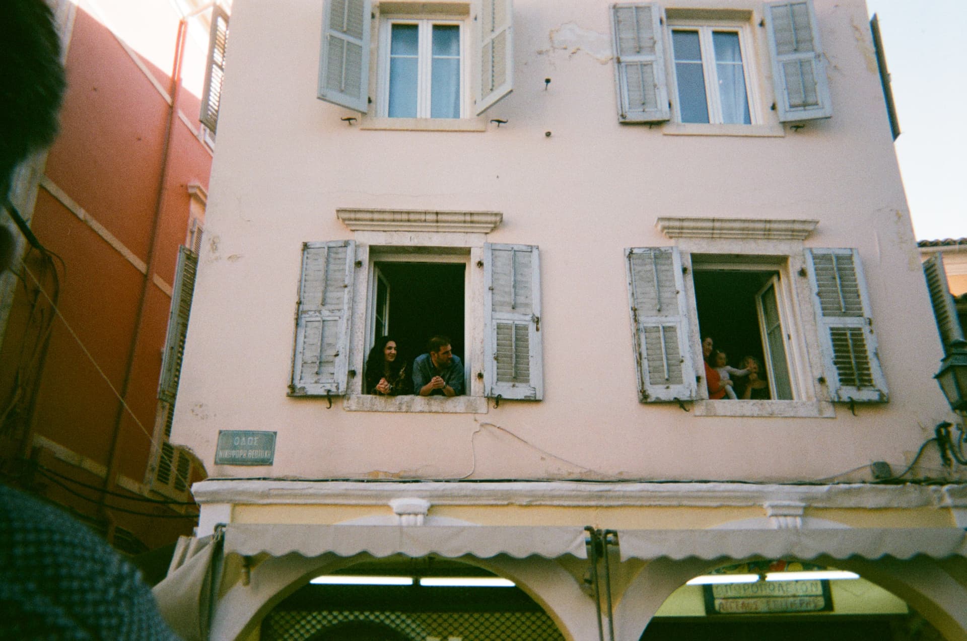 People leaning out of the shuttered windows of a pink building in an old town