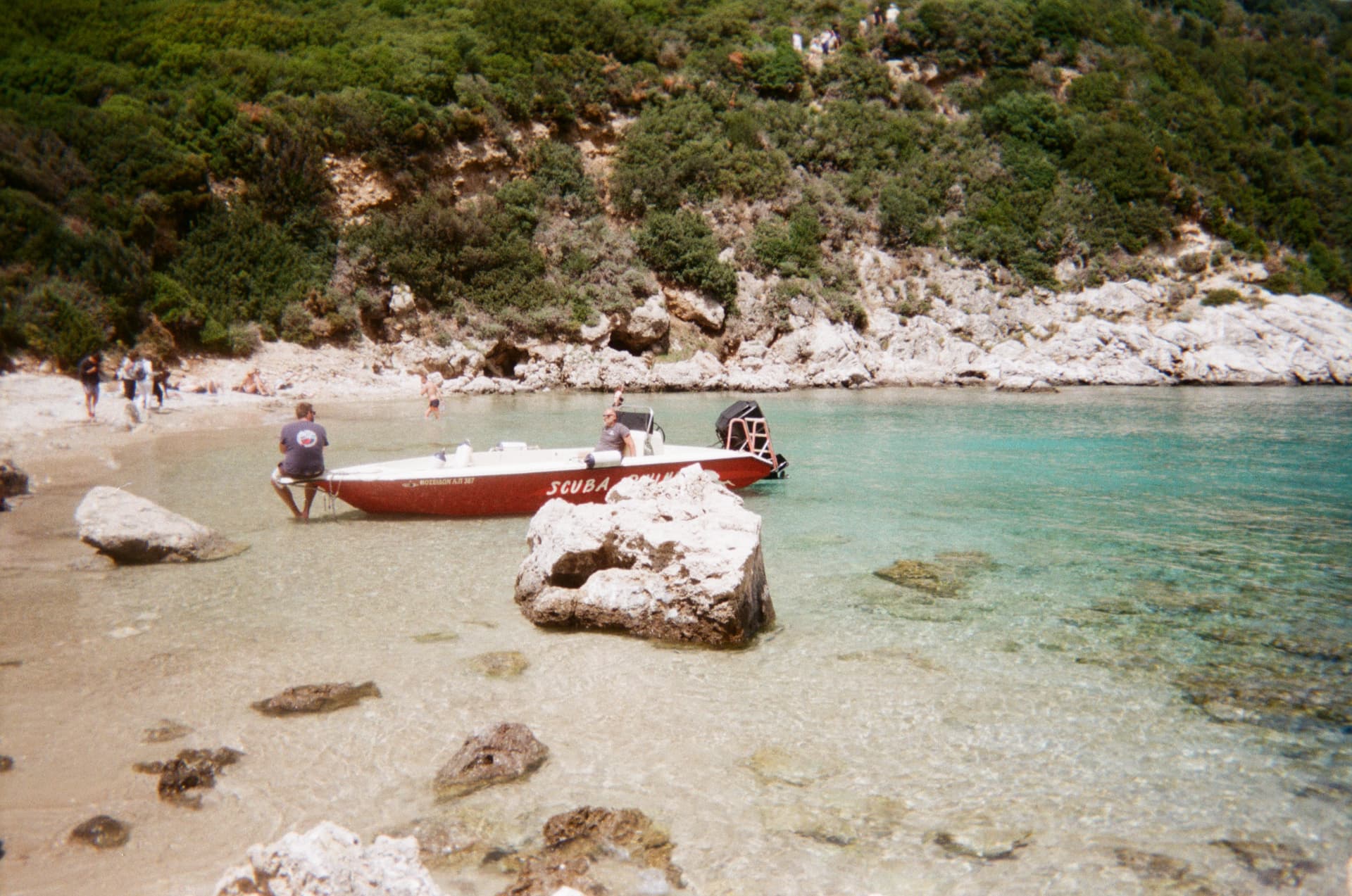 A small red boat pulled onto a turquoise pebble cove