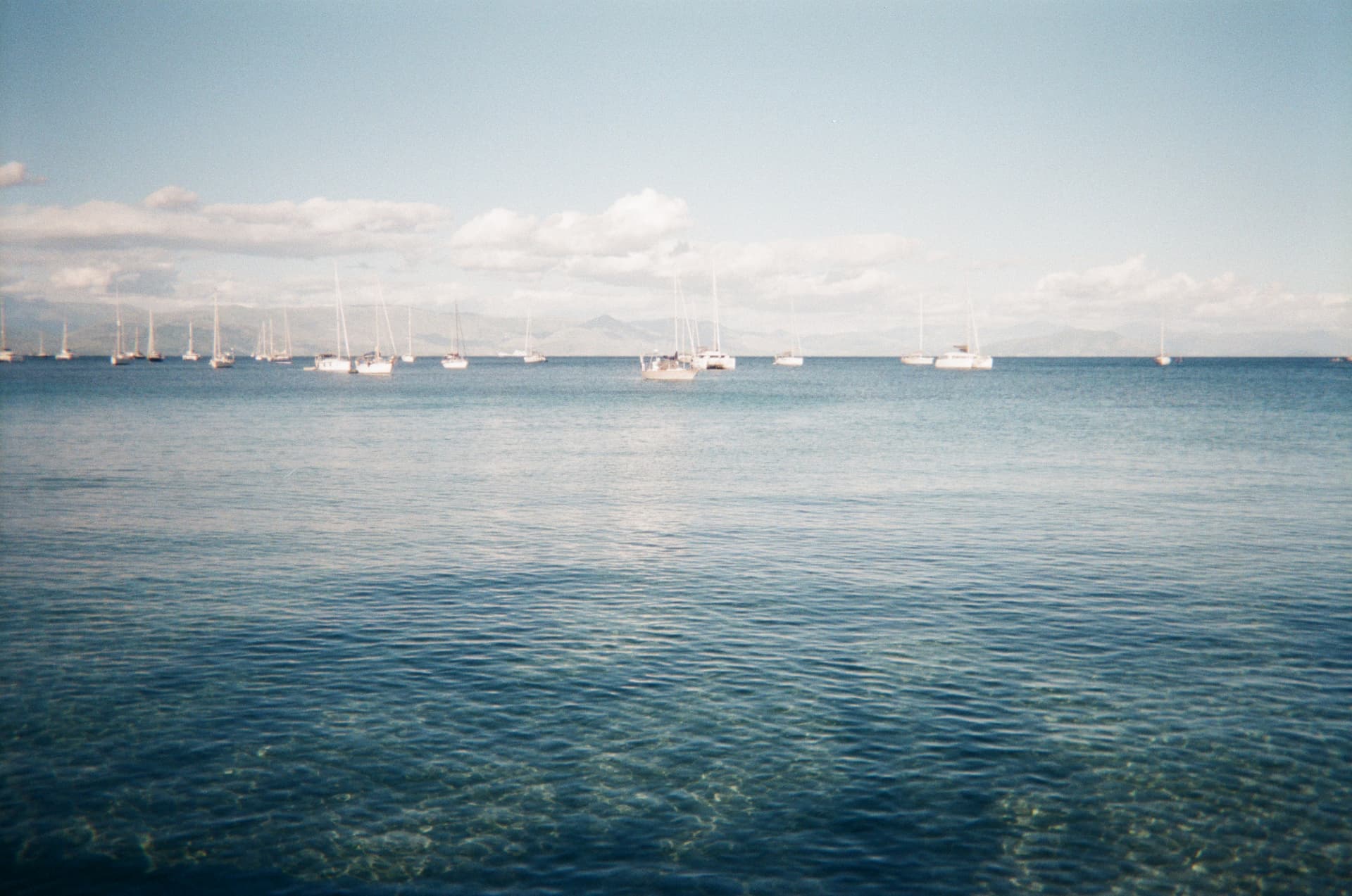 Sailboats anchored on calm blue water with distant mountains
