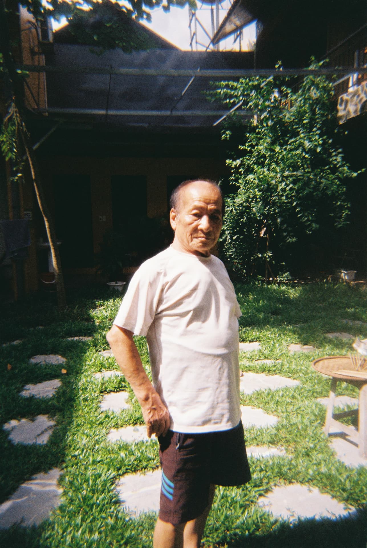 An older man standing in a sunlit green courtyard